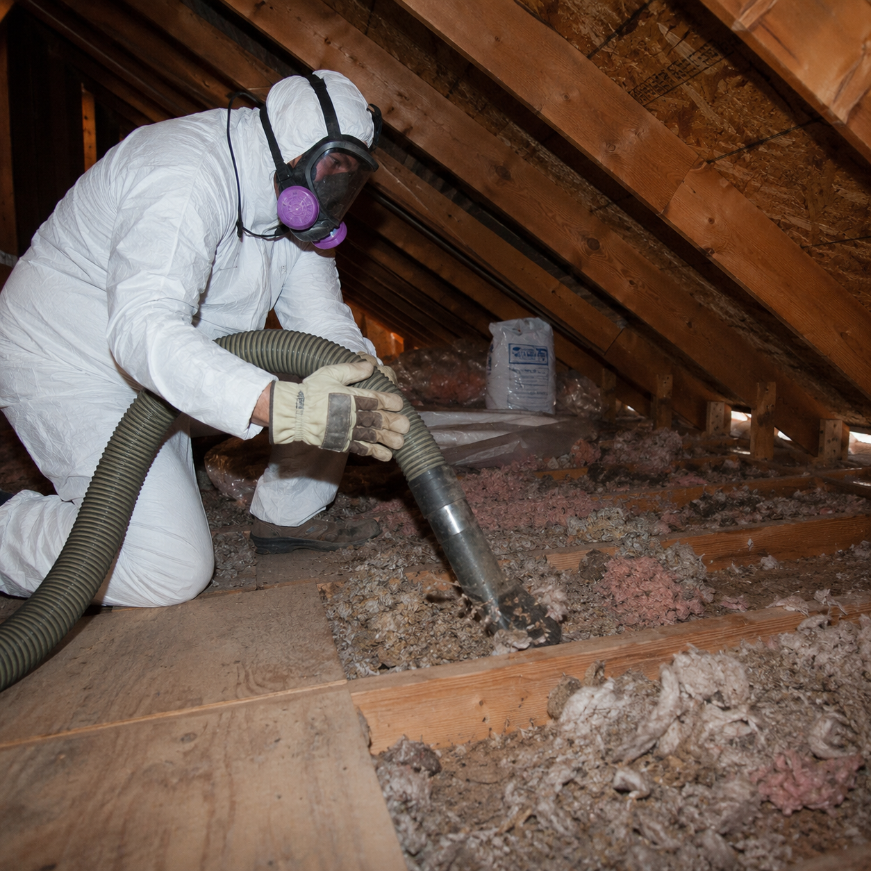 Technician in protective suit removing old attic insulation